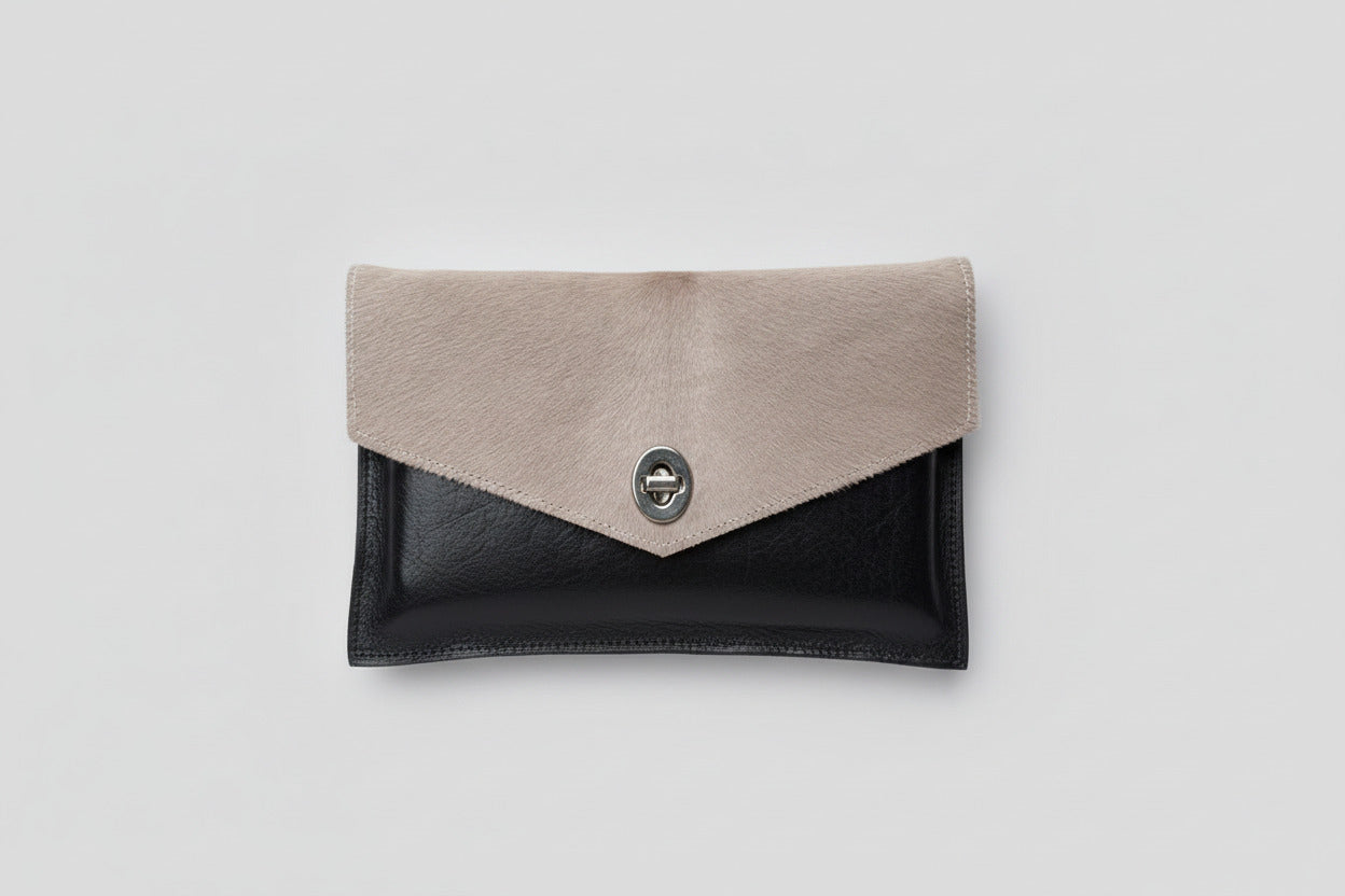 Handmade leather clutch with a metallic clasp on a tan cowhide flap